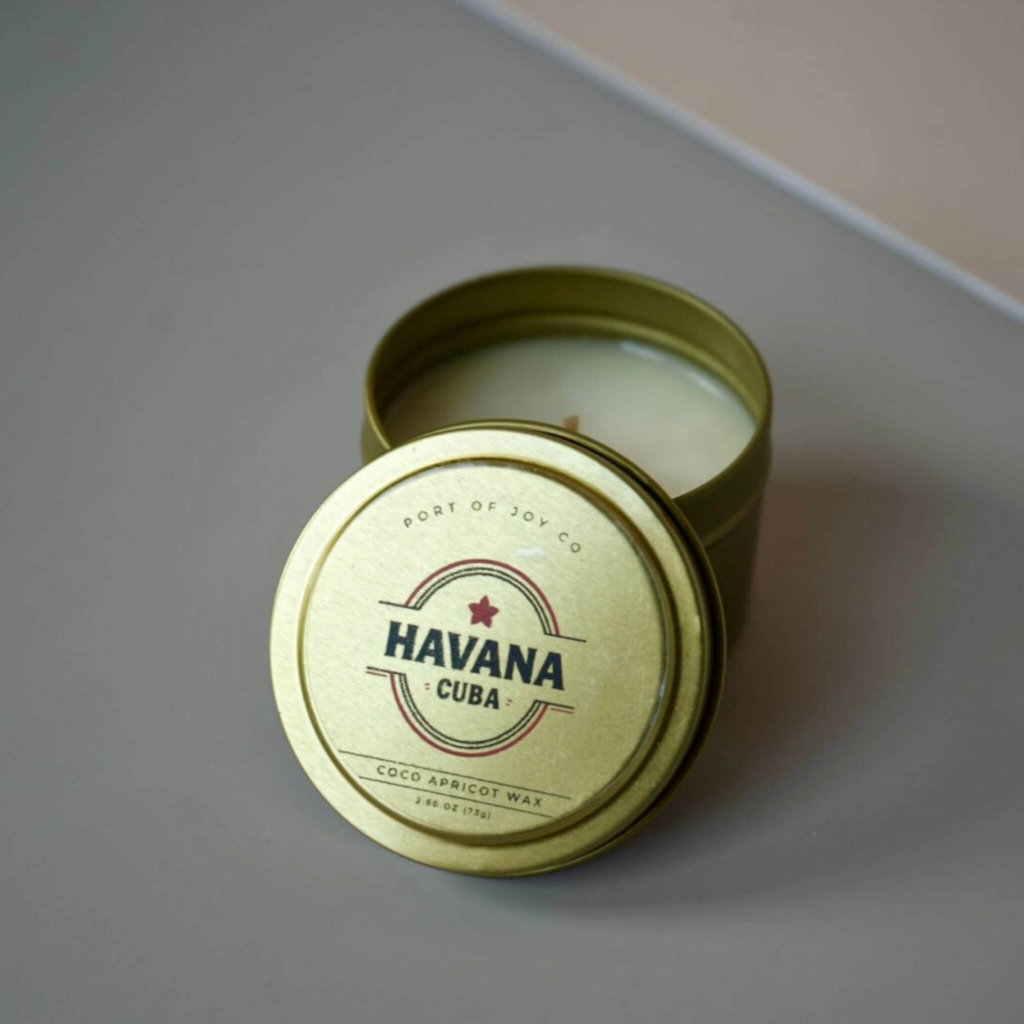 Candle in a gold tin labeled 'Havana Cuba' on a gray surface