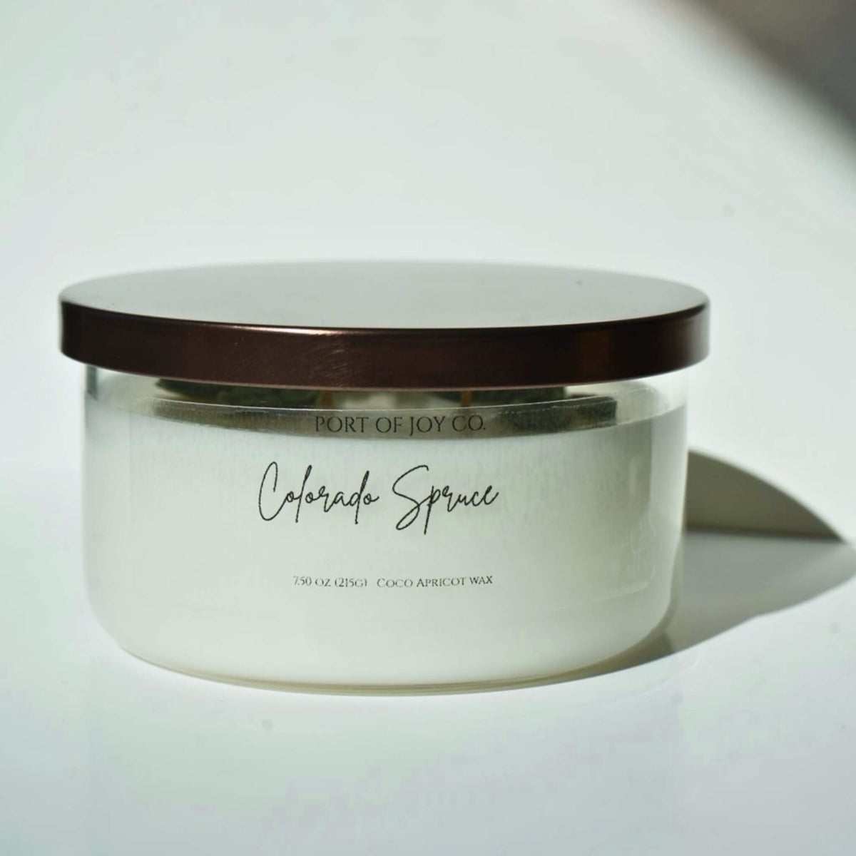 A Port of Joy Co. Colorado Spruce scented wax candle in a frosted glass jar with a bronze metallic lid