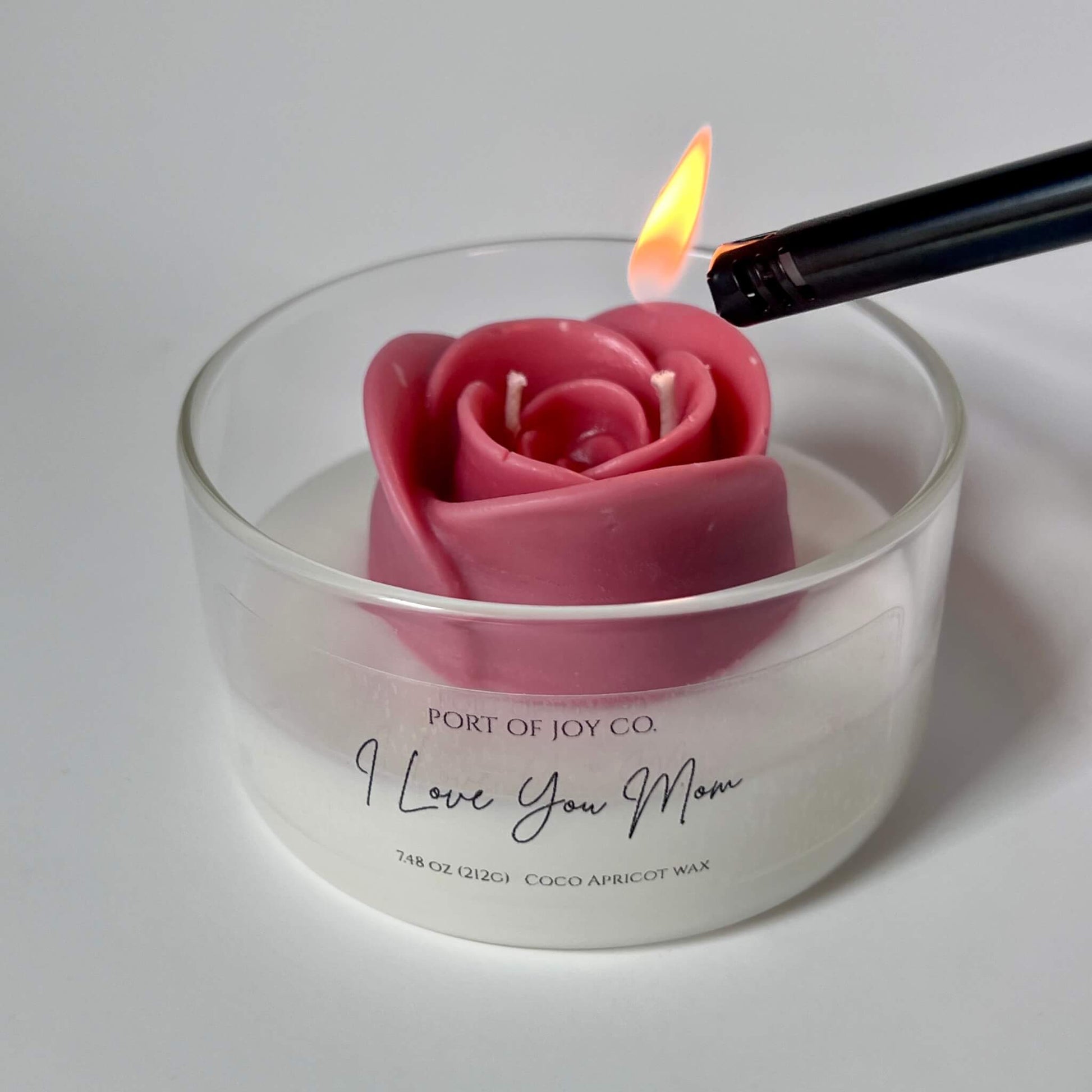 Rose-shaped candle being lit in a glass jar with 'Port of Joy Co.' branding.