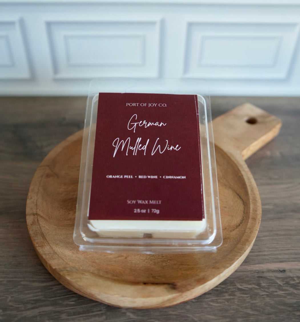 A packaged wax melt from Port of Joy Co. labeled 'German Mulled Wine' sits on a round wooden serving board.