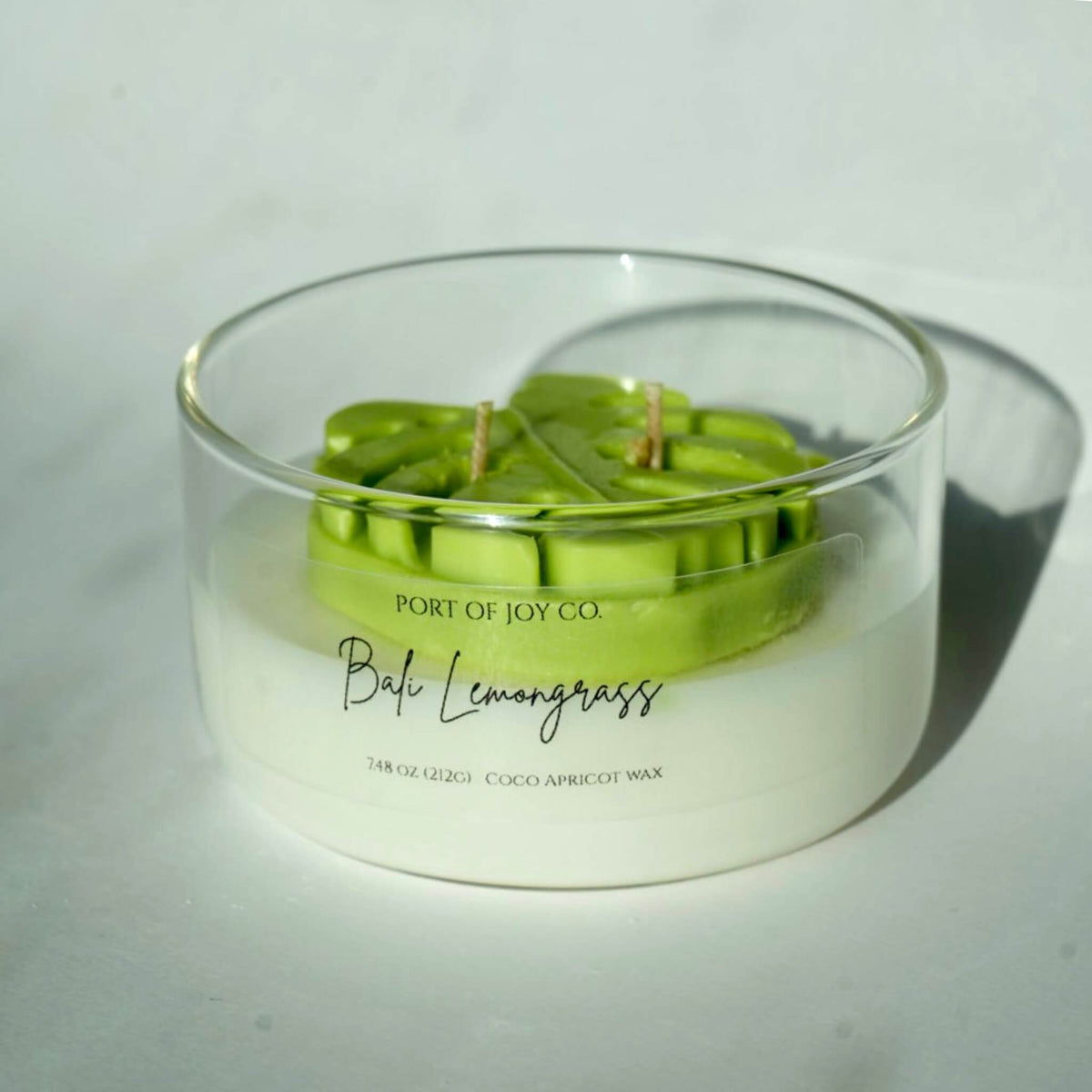 Bali lemongrass 2-wick scented candle in clear glass jar. candle in a glass vessel with a mostera leaf on top.