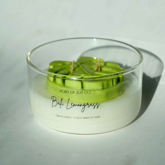handmade in usa bali lemongrass glass candle. candle in a glass vessel with a mostera leaf on top.