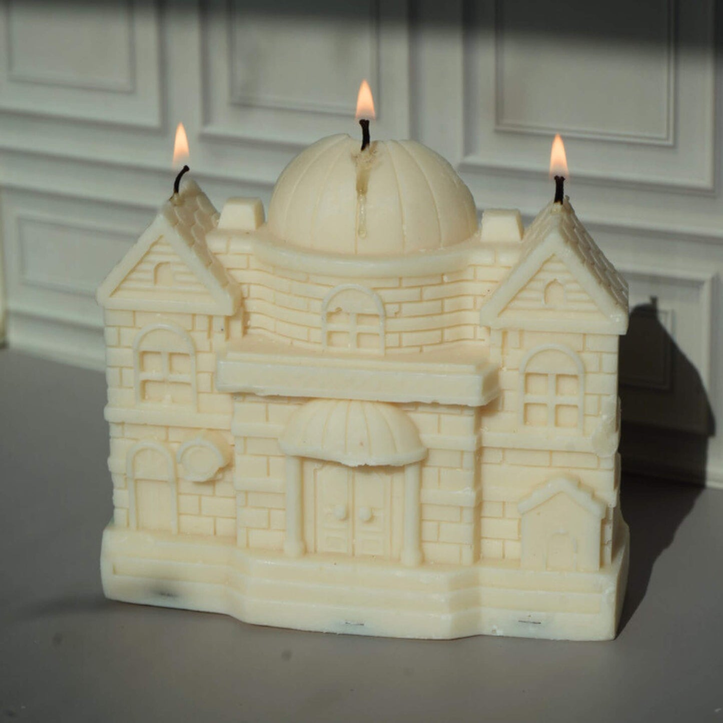 Candle shaped like a castle with three lit wicks against a neutral background