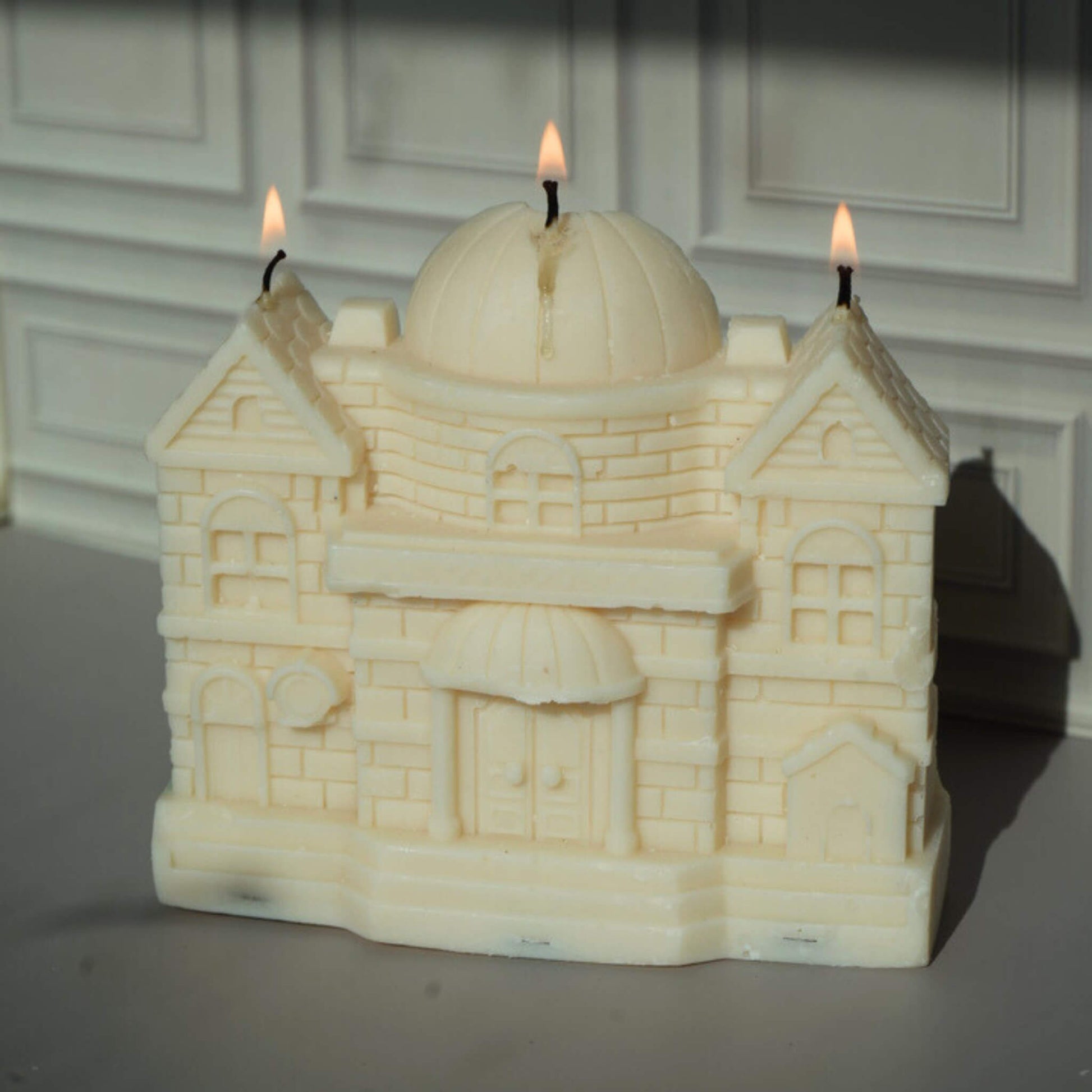 Candle shaped like a castle with three lit wicks against a neutral background