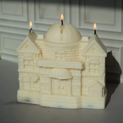 Candle shaped like a castle with three lit wicks against a neutral background