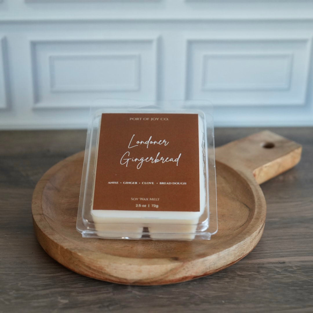 A packaged wax melt product labeled 'Londoner Gingerbread' by Port of Joy Co, placed on a round wooden serving board