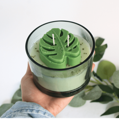 Hand holding a handmade candle with leaf-shaped wick holder against a white background.
