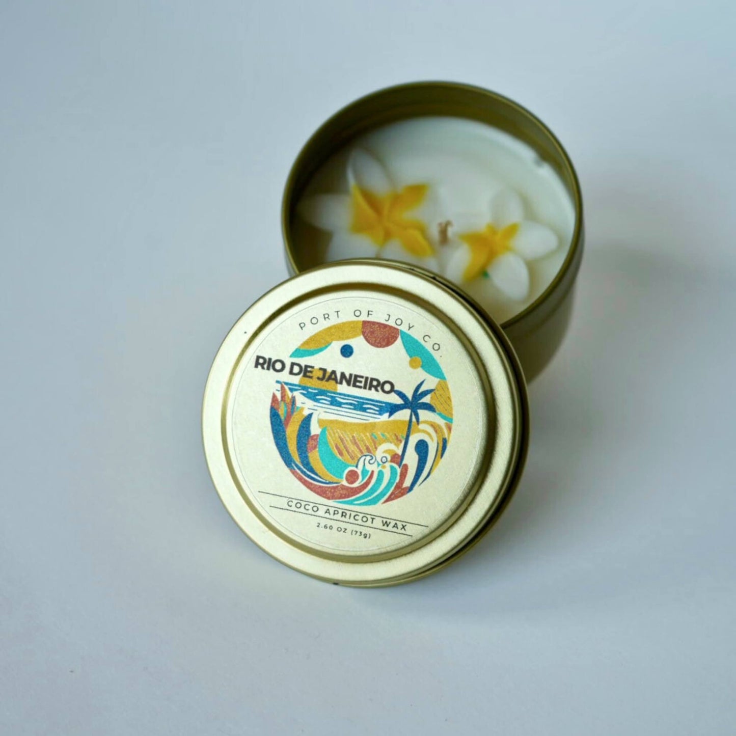 Candle in a tin with 'Rio de Janeiro' design on the lid against a light gray background