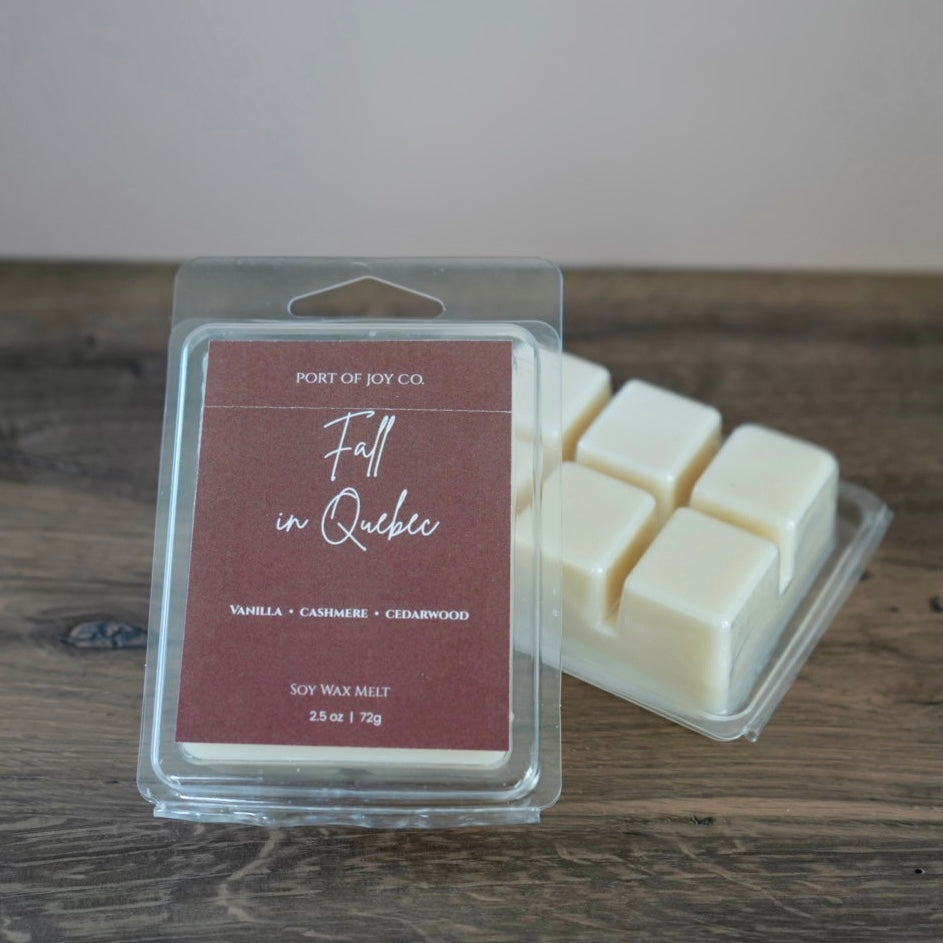 Port of Joy Co. 'Fall in Quebec' soy wax melt in a clear clamshell package with a dusty rose label, shown next to several off-white wax cubes on a rustic wooden surface.