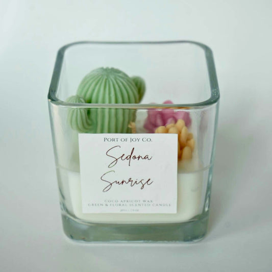 Candle in a glass container with decorative cactusand succulents on a light background
