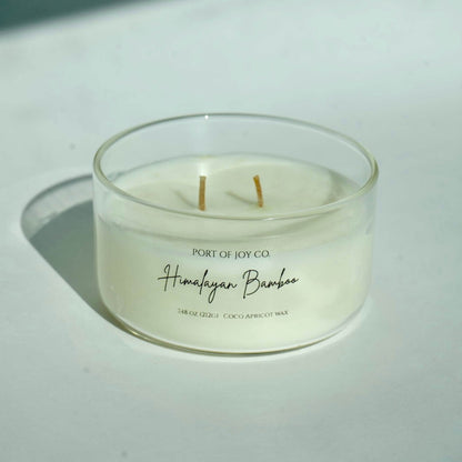 Candle in a glass jar labeled 'Himalayan Bamboo' from Port of Joy Co. on a light background