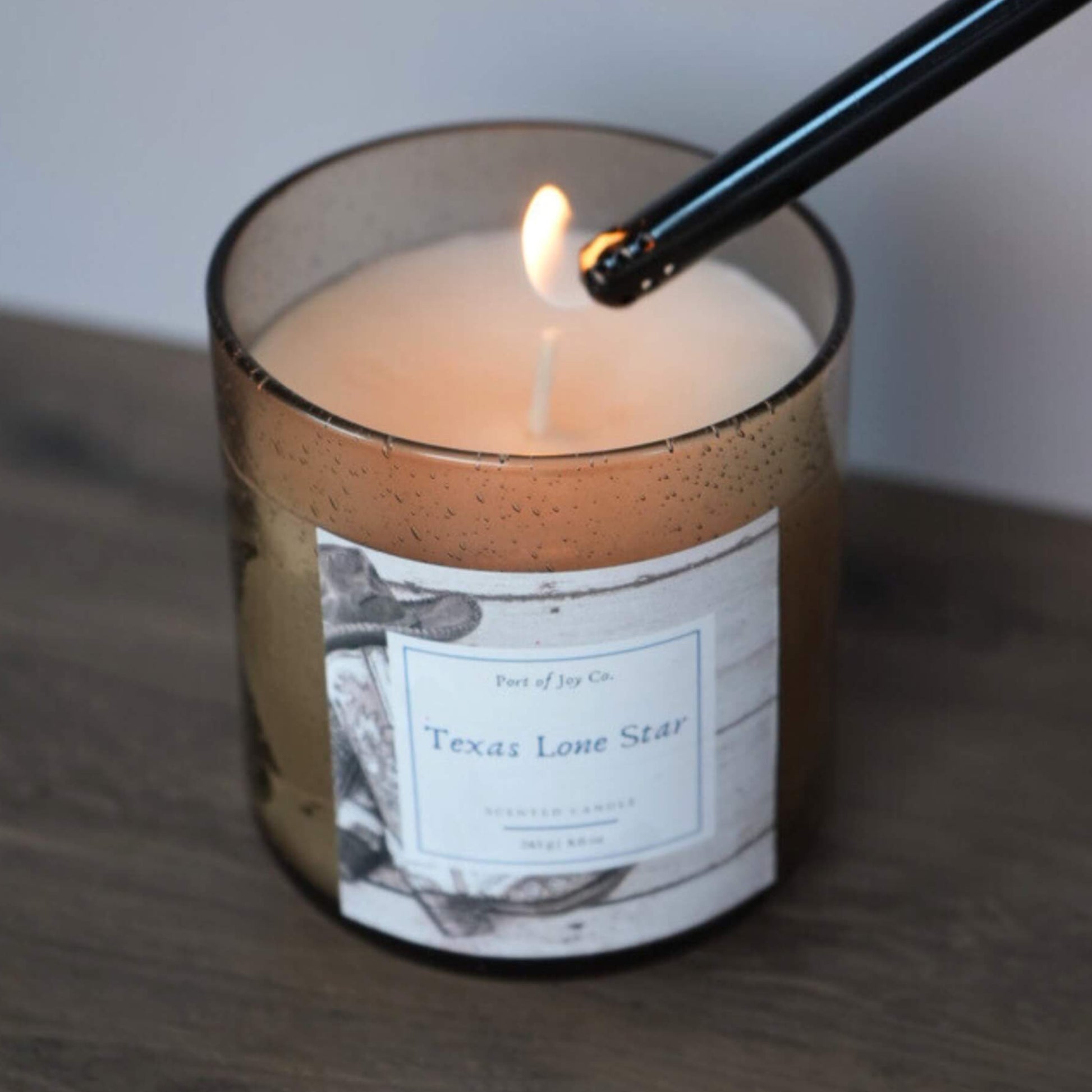 Candle labeled 'Texas Lone Star' being lit with a match on a wooden surface.