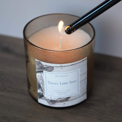 Candle labeled 'Texas Lone Star' being lit with a match on a wooden surface.