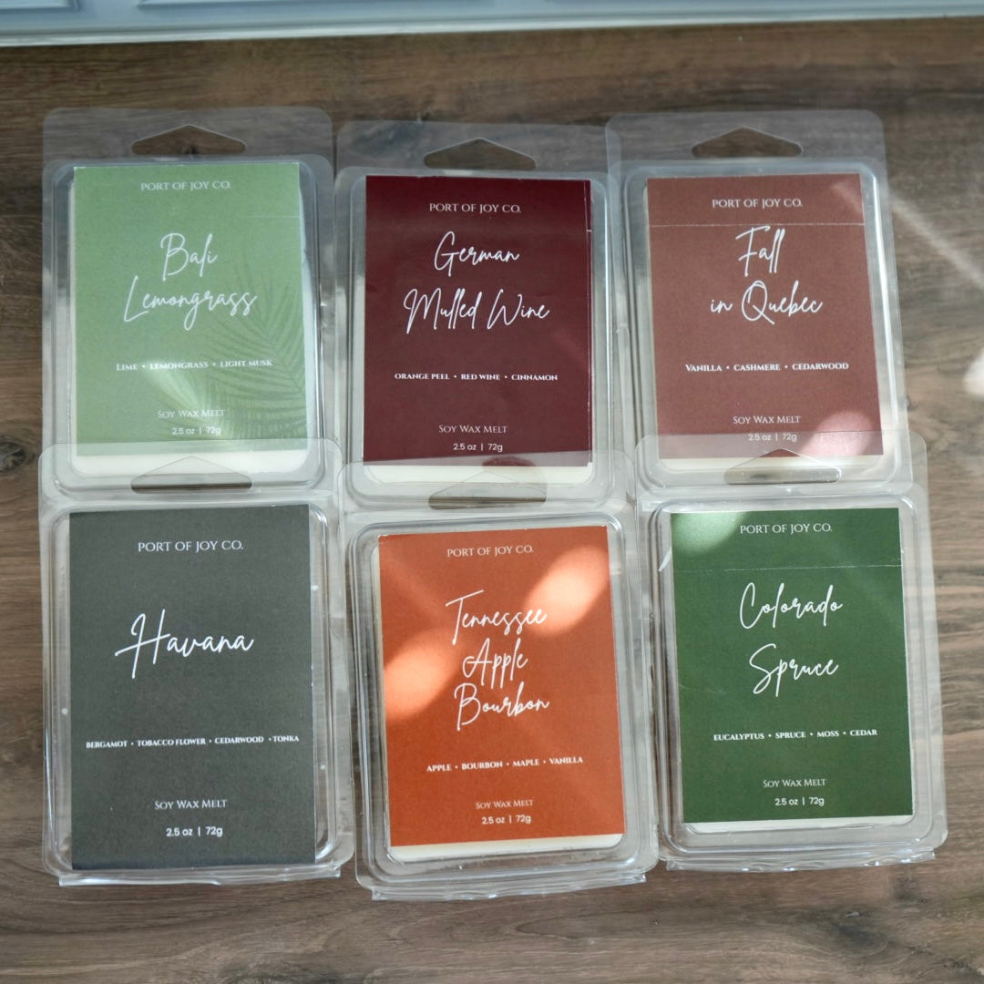 Six Port of Joy Co. soy wax melts in clear plastic clamshell packaging arranged in a 2x3 grid on a dark wooden surface.