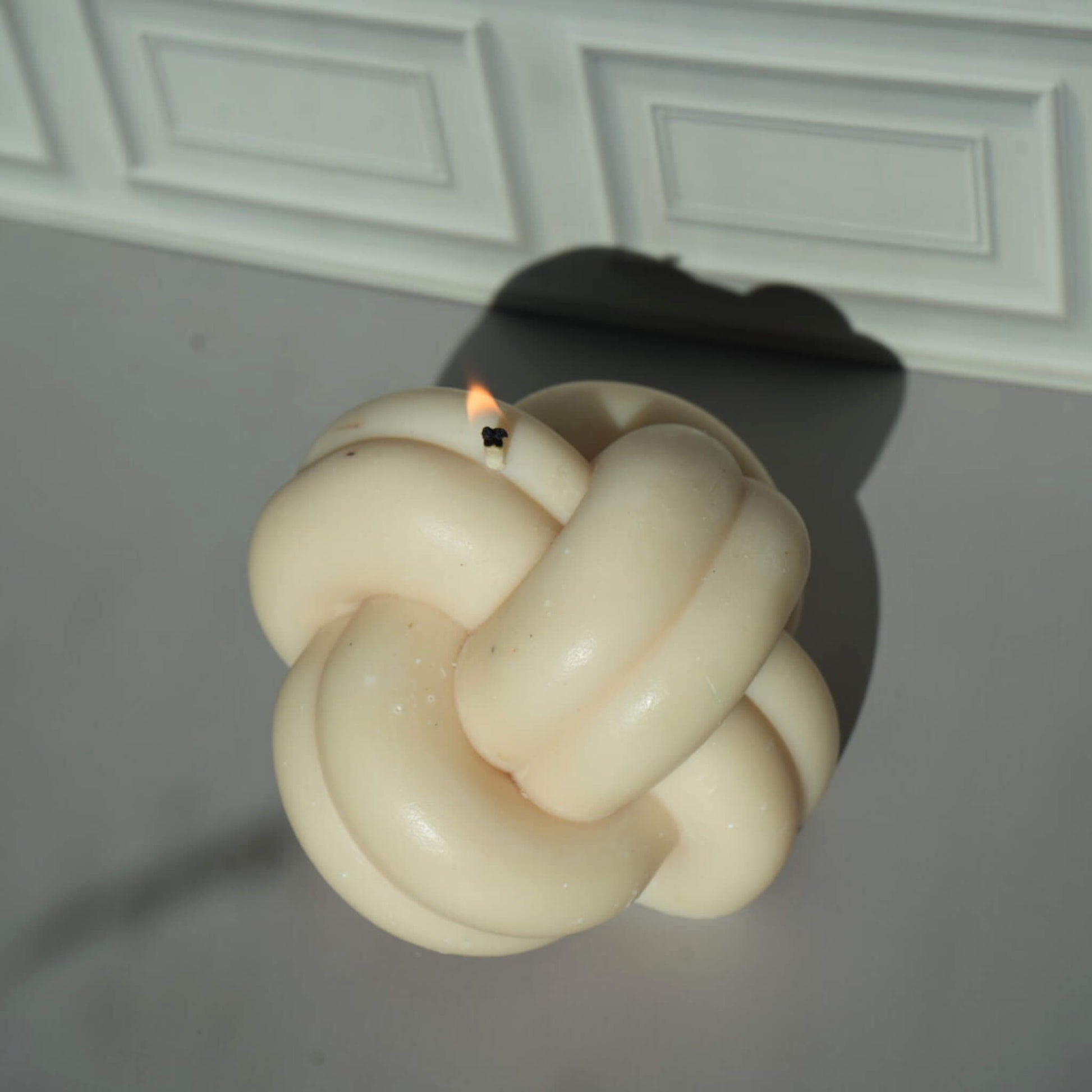 Knot-shaped candle with a flame on a plain background