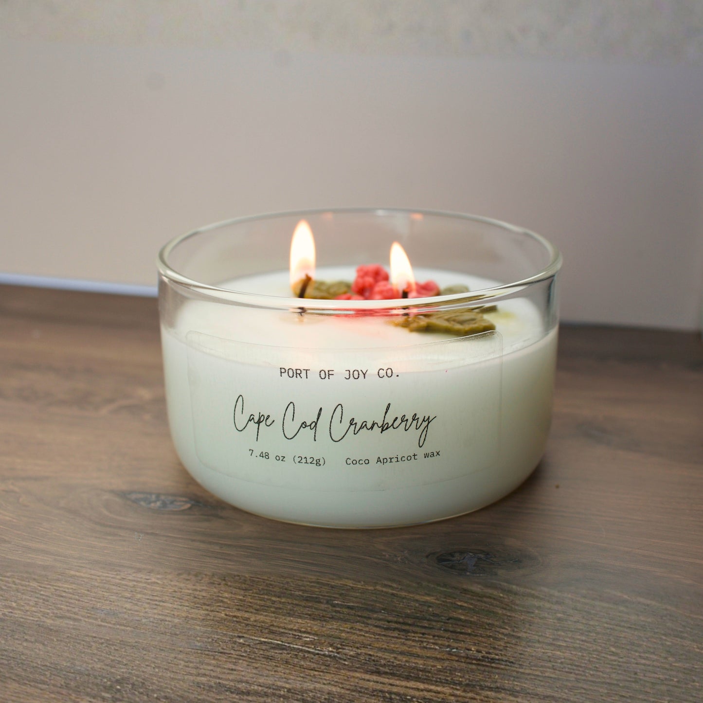 Cape Cod Cranberry candle in a clear glass jar with double wicks, hand-poured and elegantly designed. A cozy holiday scent and perfect Christmas gift for her. image shows candle light up.