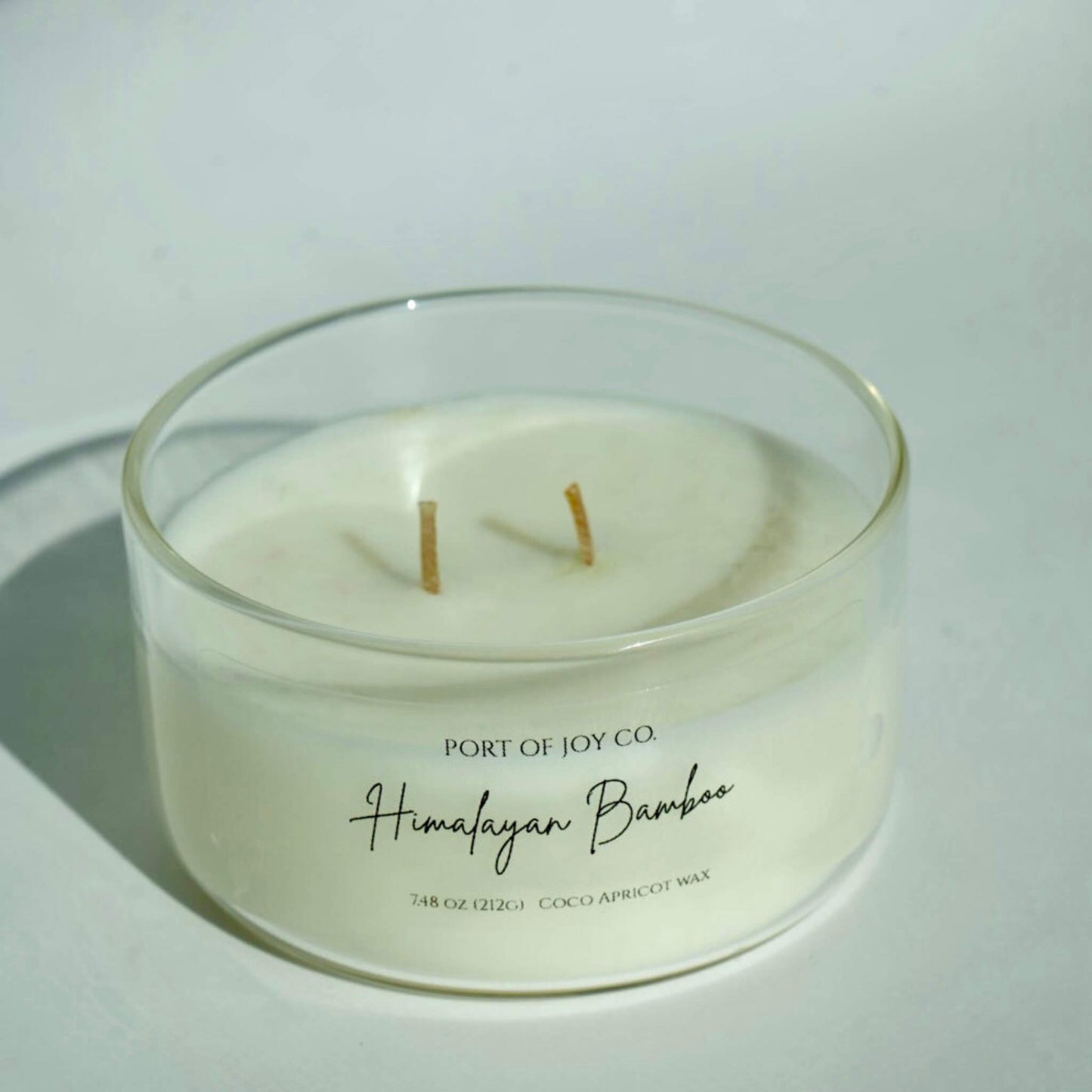 White candle in a glass container with 'Port of Joy Co.' branding on a light background