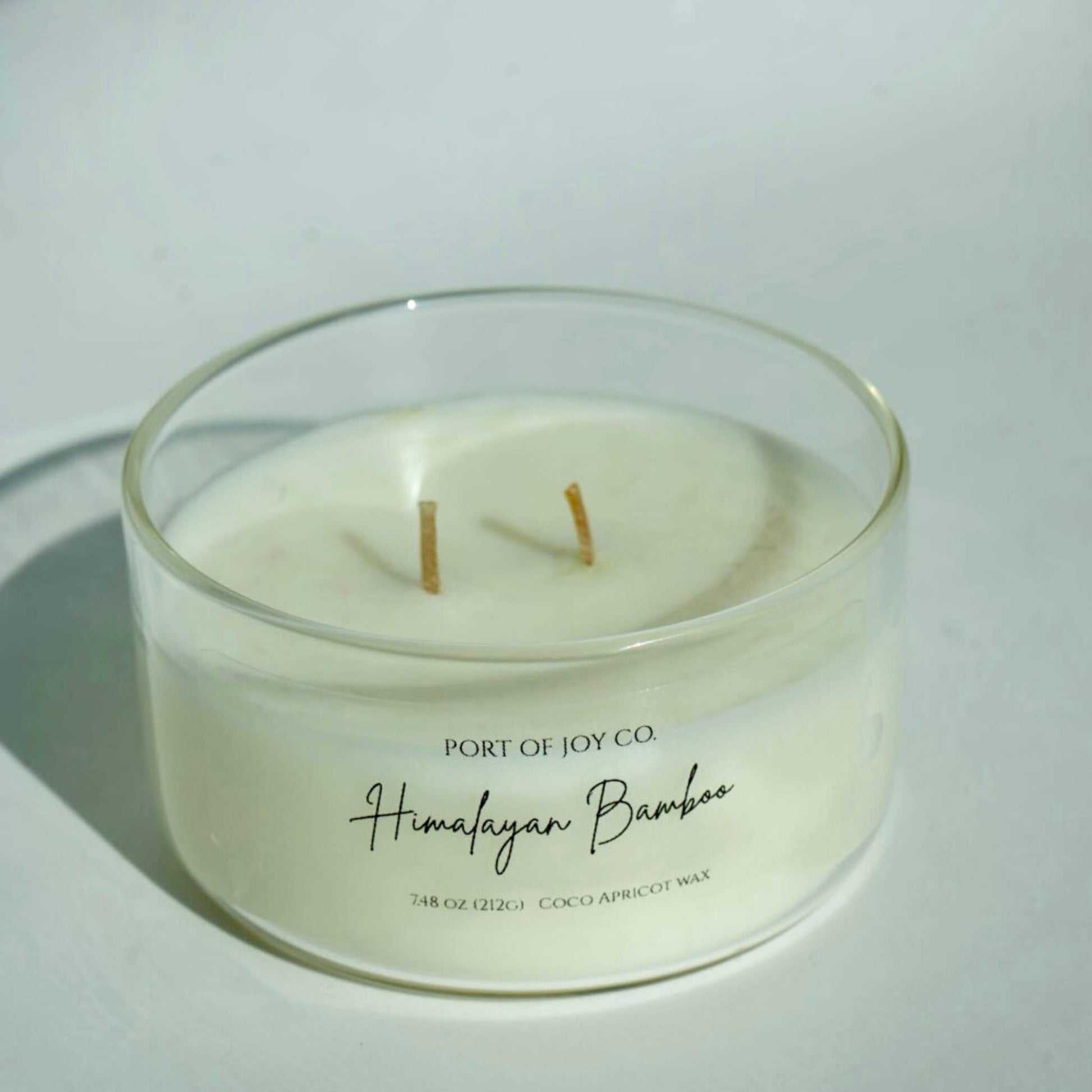 White candle in a glass container with 'Port of Joy Co.' branding on a light background