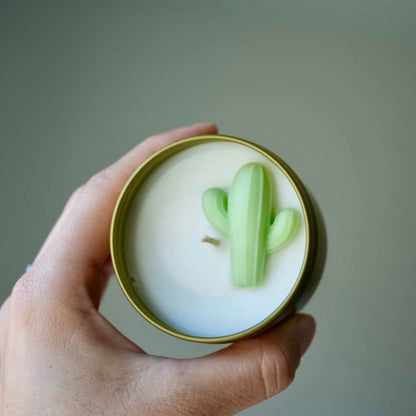 Hand holding a candle with a cactus design on a plain background