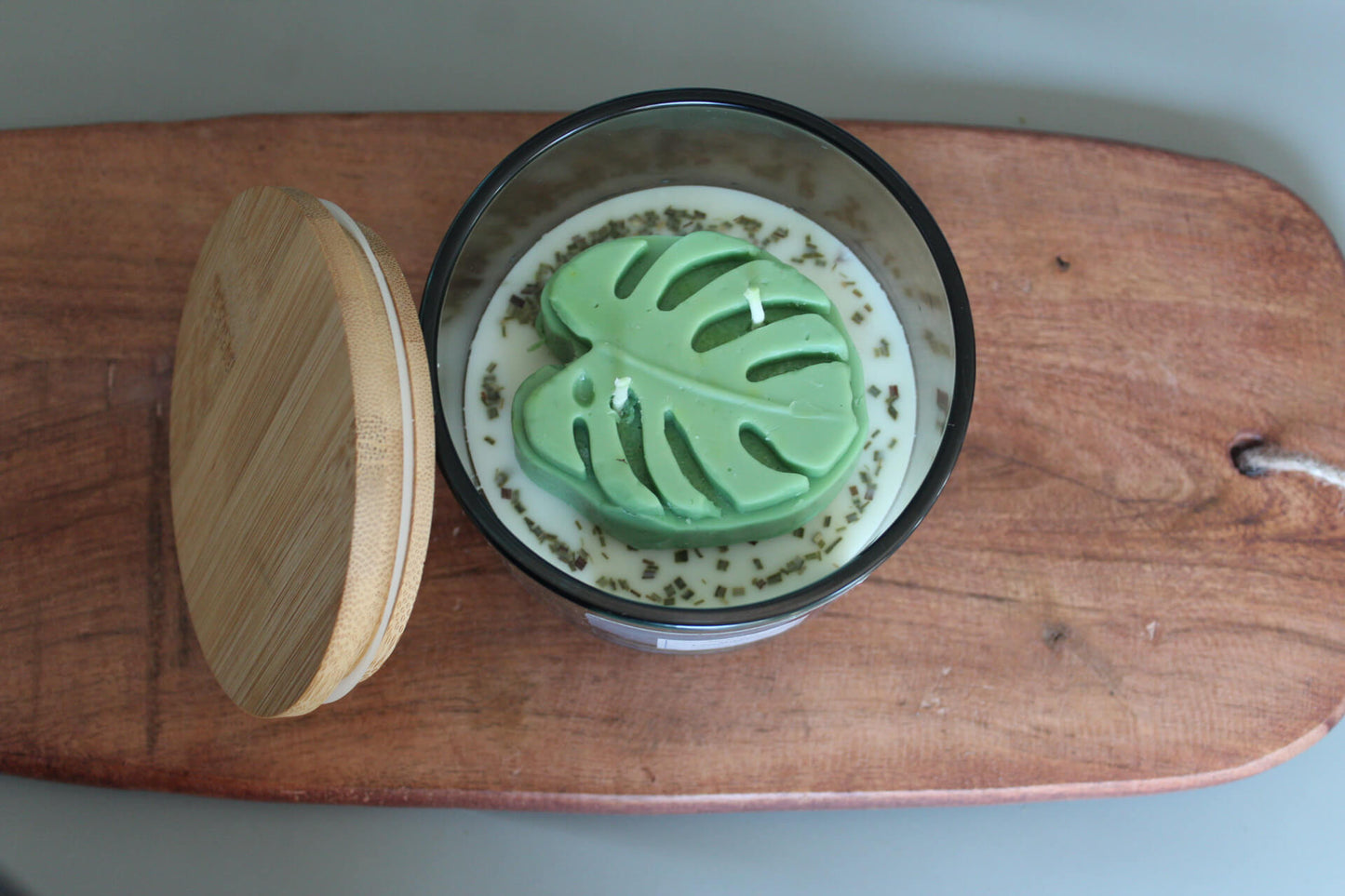 coconut apricot wax Candle with green leaf-shaped embed on a wooden board. 