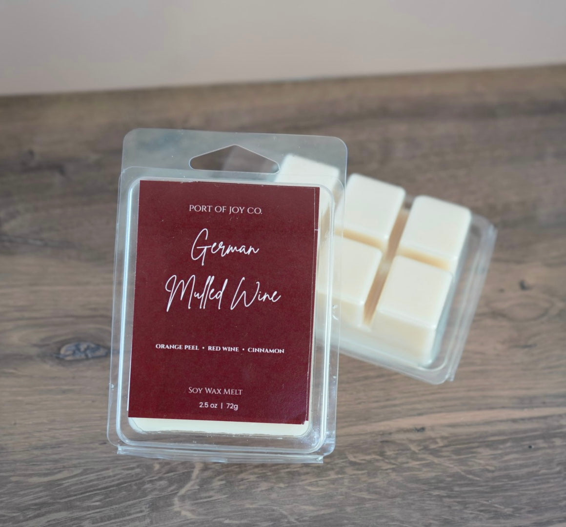 Port of Joy Co. German Mulled Wine scented soy wax melts in a clear clamshell container, with a second container of white wax cubes behind it, set on a rustic wooden tabletop.